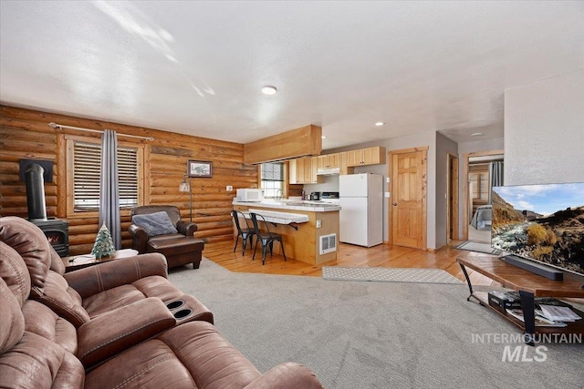 living room featuring log walls, light wood-type flooring, and a wood stove