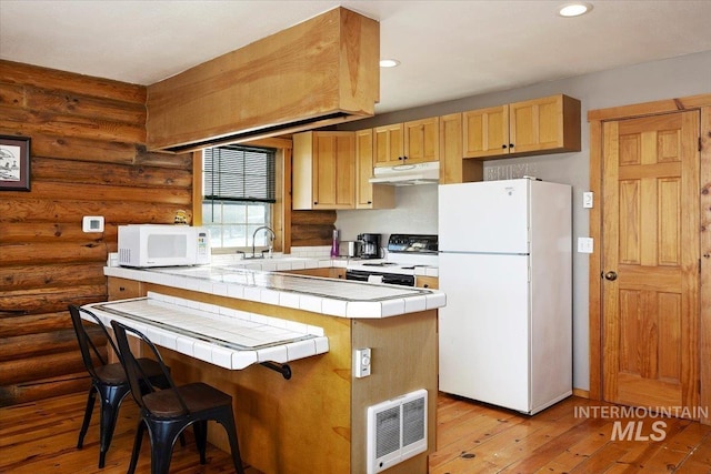 kitchen featuring hardwood / wood-style floors, white appliances, tile counters, and a kitchen bar