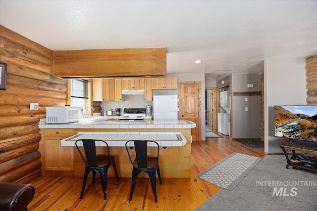 kitchen featuring white appliances, tile counters, rustic walls, and light wood-type flooring