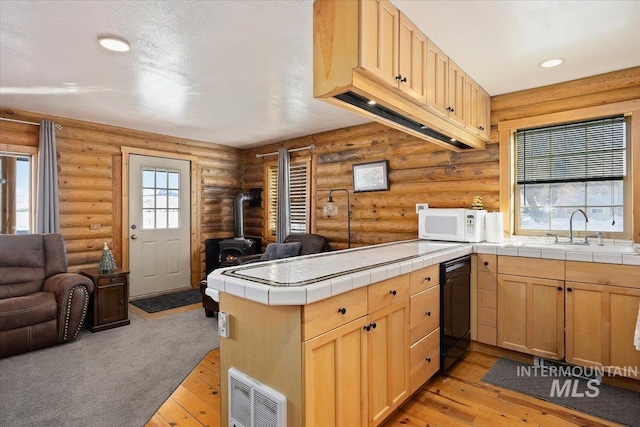 kitchen featuring dishwasher, a wood stove, tile counters, light hardwood / wood-style floors, and kitchen peninsula