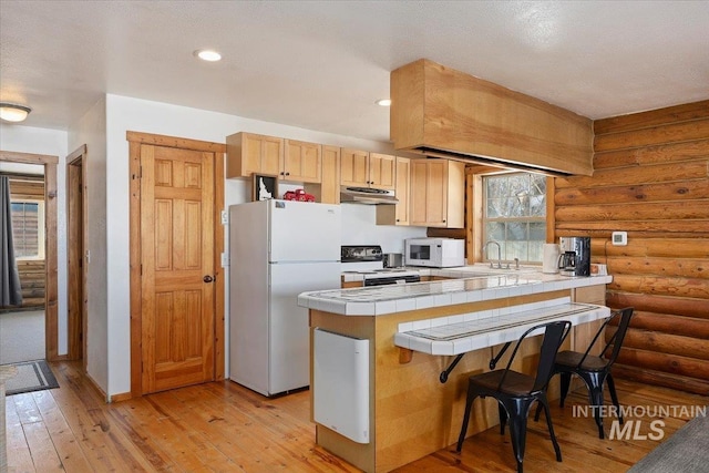 kitchen with rustic walls, a breakfast bar area, light wood-type flooring, tile counters, and white appliances