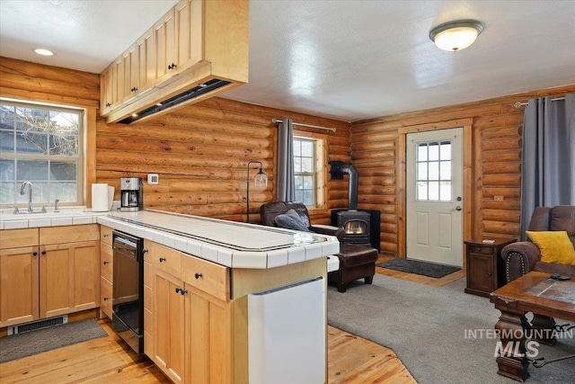 kitchen with dishwashing machine, light hardwood / wood-style flooring, tile countertops, kitchen peninsula, and a wood stove