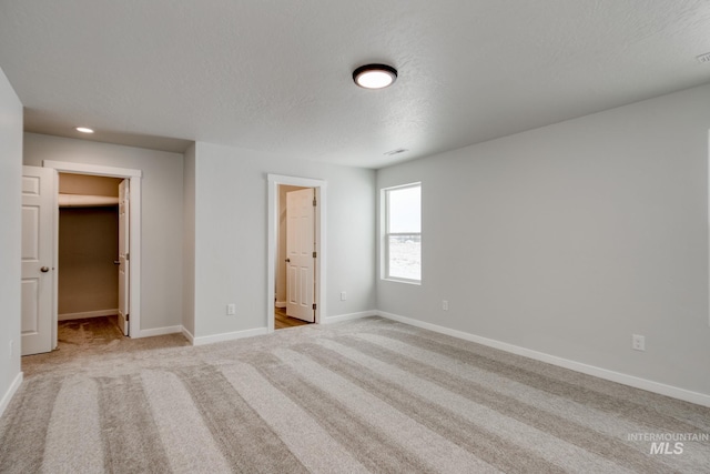 unfurnished bedroom featuring light colored carpet, baseboards, a walk in closet, and recessed lighting