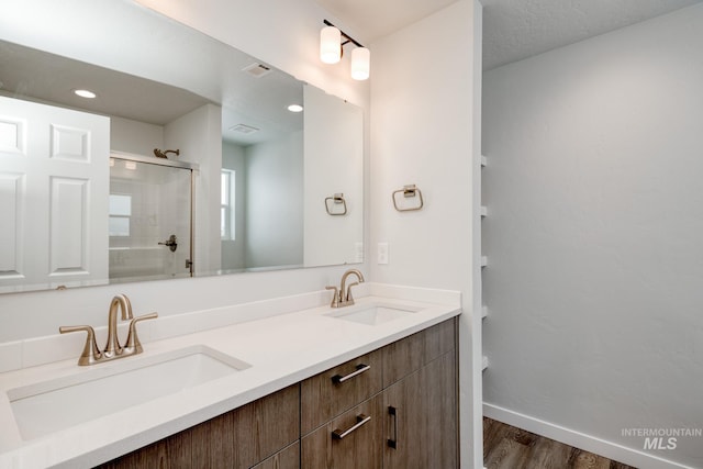 full bath featuring a shower with door, double vanity, a sink, and wood finished floors