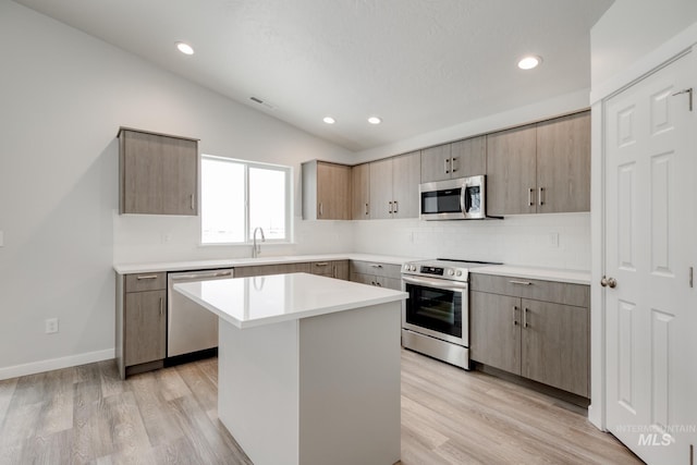 kitchen featuring lofted ceiling, visible vents, light wood finished floors, decorative backsplash, and appliances with stainless steel finishes
