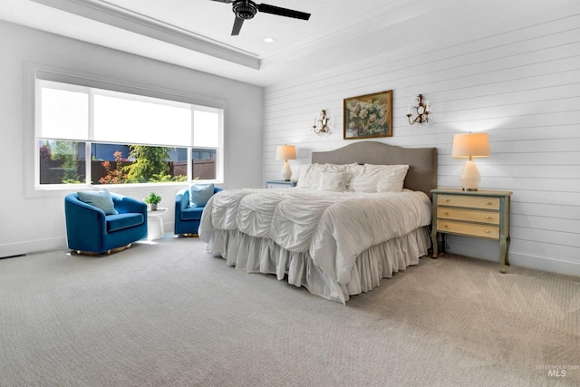 bedroom featuring light colored carpet, a tray ceiling, wooden walls, ceiling fan, and baseboards