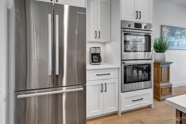 kitchen with appliances with stainless steel finishes, light countertops, light wood-style flooring, white cabinetry, and backsplash