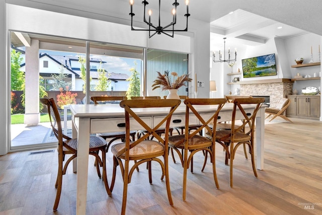 dining area with a chandelier, light wood-style flooring, a fireplace, and beamed ceiling