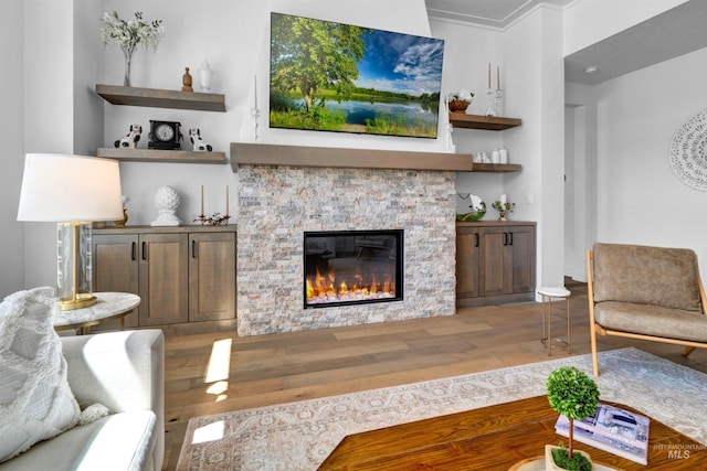 living room with wood finished floors, a stone fireplace, crown molding, and baseboards