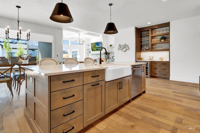 kitchen with a chandelier, a sink, stainless steel dishwasher, light countertops, and light wood-type flooring