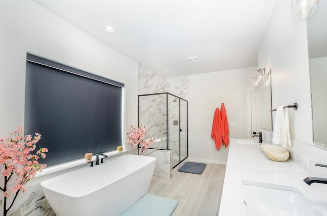 bathroom with shower with separate bathtub, hardwood / wood-style floors, oversized vanity, and double sink