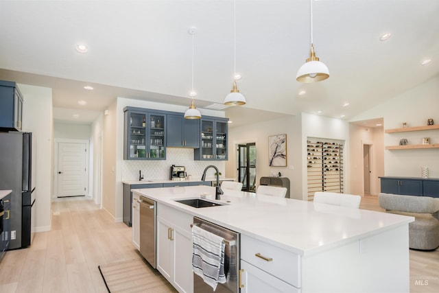 kitchen featuring stainless steel appliances, blue cabinets, an island with sink, light wood-type flooring, and sink