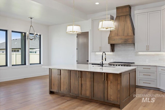 1967 Red Rock Way, Twin Falls, ID 83301 - kitchen with custom exhaust hood, light wood-type flooring, tasteful backsplash, an island with sink, and a chandelier