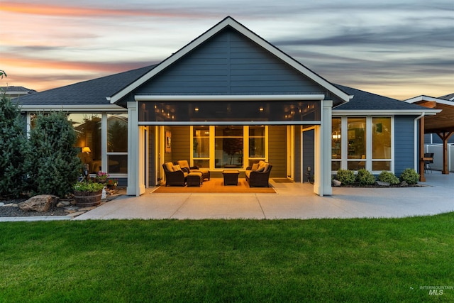 back house at dusk featuring a sunroom, an outdoor living space, a patio, and a lawn