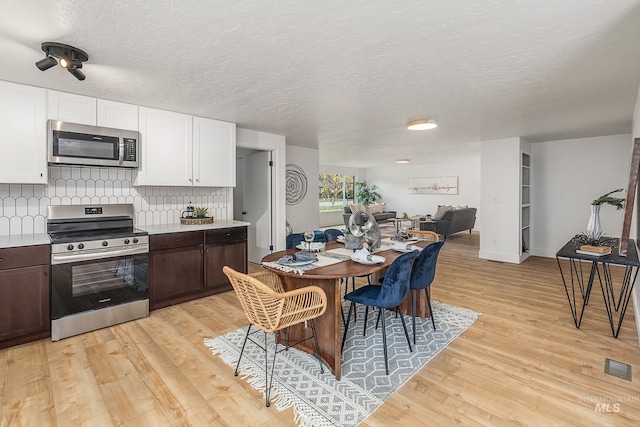 kitchen featuring appliances with stainless steel finishes, backsplash, dark brown cabinets, white cabinets, and a textured ceiling