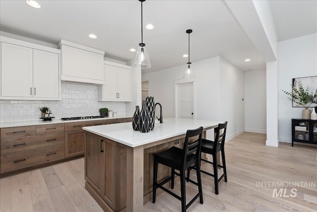 7625 W Whisper Ridge Dr, Meridian, ID 83646 - kitchen featuring light wood-style floors, backsplash, light countertops, an island with sink, and white cabinetry