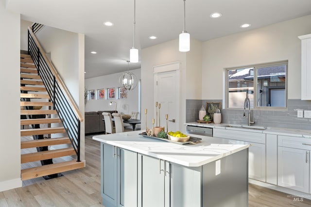 kitchen featuring light stone counters, a kitchen island, pendant lighting, sink, and light hardwood / wood-style flooring