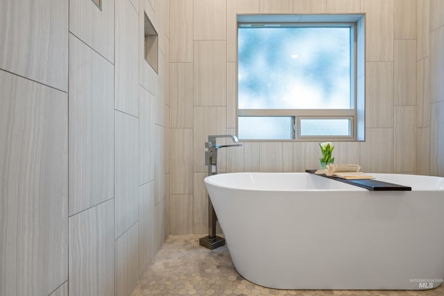 bathroom with tile walls, a washtub, and tile patterned floors