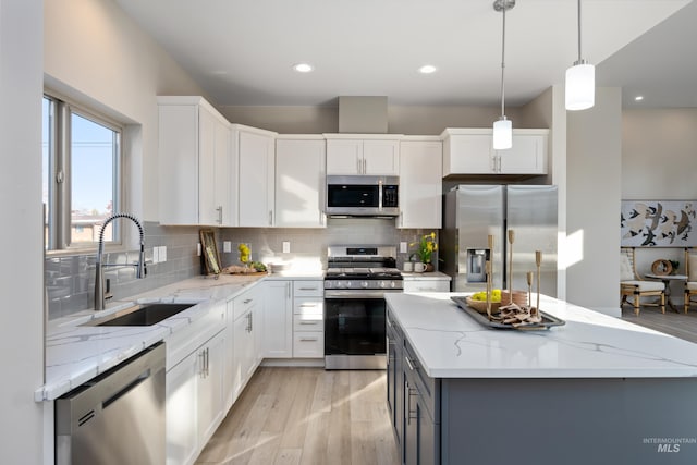 kitchen featuring stainless steel appliances, hanging light fixtures, white cabinets, and light hardwood / wood-style flooring