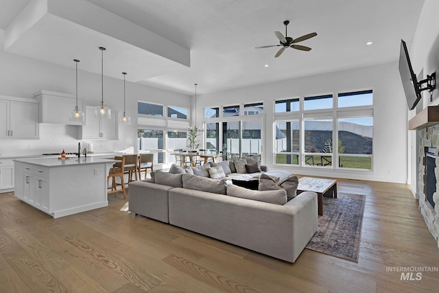 living room with a stone fireplace, ceiling fan, and light wood-type flooring