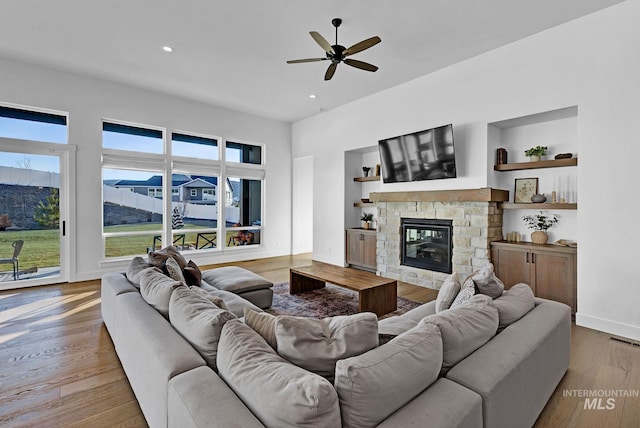 living room featuring ceiling fan, built in shelves, a fireplace, and wood-type flooring