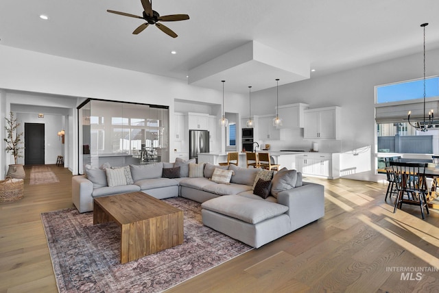 living room featuring ceiling fan with notable chandelier, light wood-type flooring, and a high ceiling