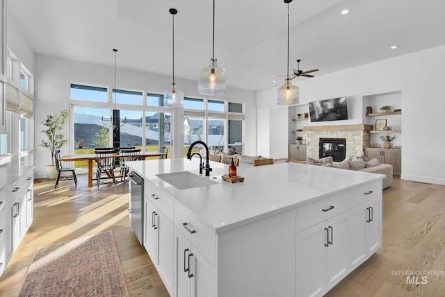 kitchen with sink, a center island with sink, light wood-type flooring, pendant lighting, and white cabinets