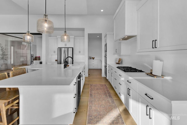 kitchen with appliances with stainless steel finishes, a breakfast bar, decorative light fixtures, white cabinetry, and a large island with sink