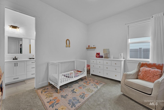 bedroom featuring light colored carpet, connected bathroom, sink, and a crib