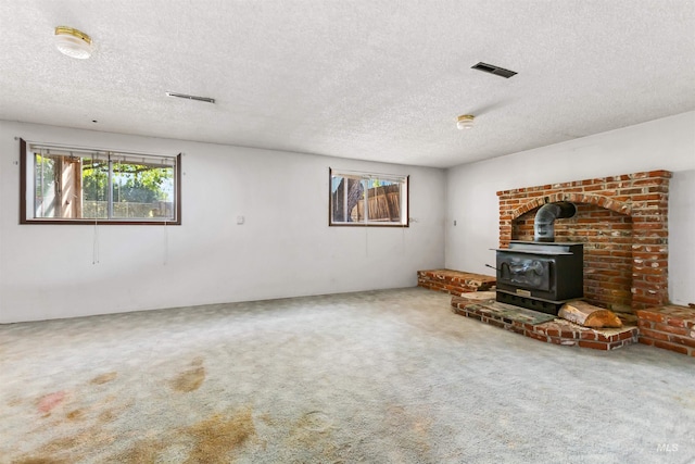 unfurnished living room featuring carpet, a wood stove, a textured ceiling, and visible vents