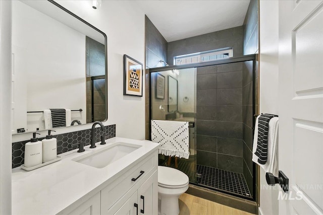 bathroom with backsplash, wood finished floors, toilet, vanity, and a stall shower