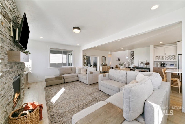 living area with baseboards, recessed lighting, a stone fireplace, and light wood-type flooring