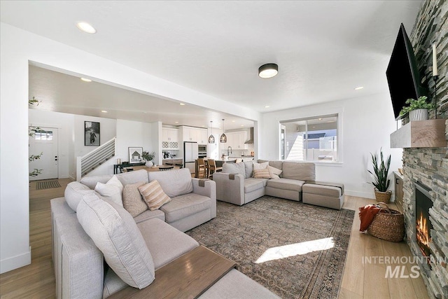 living area with a fireplace, light wood-style floors, stairway, and plenty of natural light