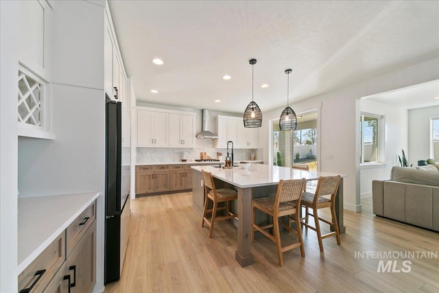 kitchen featuring plenty of natural light, a breakfast bar area, wall chimney exhaust hood, and black refrigerator