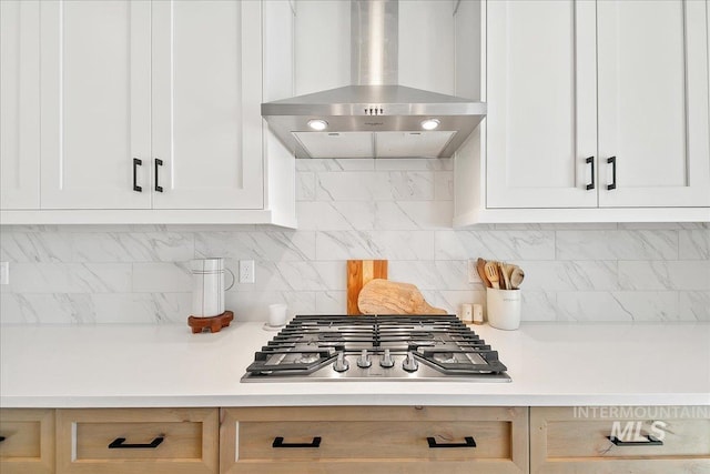 kitchen with white cabinetry, stainless steel gas stovetop, decorative backsplash, exhaust hood, and light countertops