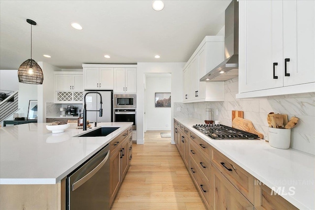 kitchen featuring wall chimney range hood, a sink, decorative backsplash, light countertops, and appliances with stainless steel finishes
