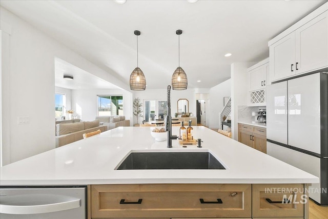 kitchen featuring light countertops, stainless steel dishwasher, a sink, freestanding refrigerator, and open floor plan