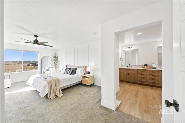 bedroom with a sink, ensuite bathroom, ceiling fan, light colored carpet, and baseboards