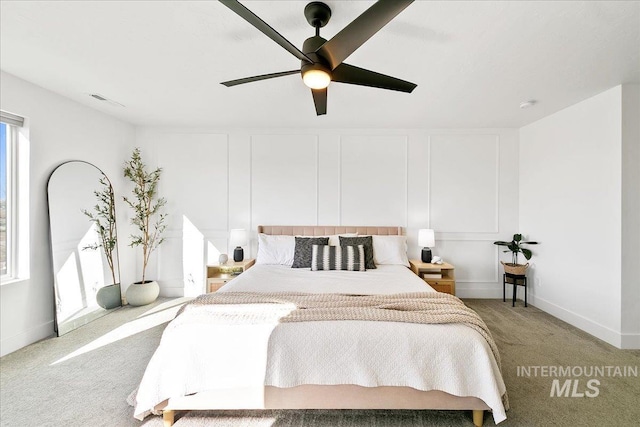 bedroom featuring visible vents, a ceiling fan, light carpet, a decorative wall, and baseboards