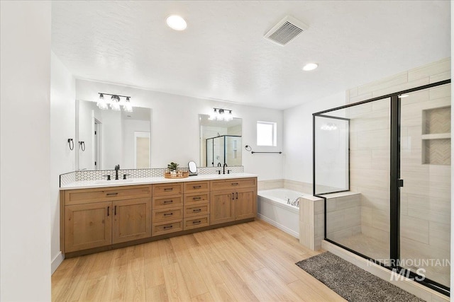 bathroom with wood finished floors, visible vents, a sink, a bath, and a stall shower