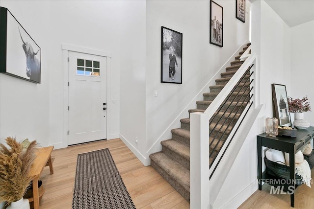 entryway with baseboards, stairs, and light wood finished floors