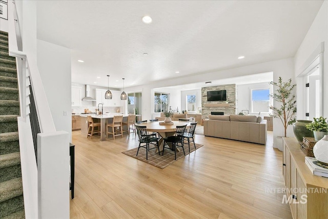 dining area featuring recessed lighting, a stone fireplace, stairs, and light wood-type flooring