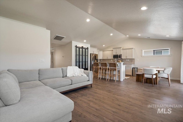 7682 W Itasco Dr, Boise, ID 83709 - living room featuring a barn door, vaulted ceiling, dark wood-style flooring, recessed lighting, and a textured ceiling