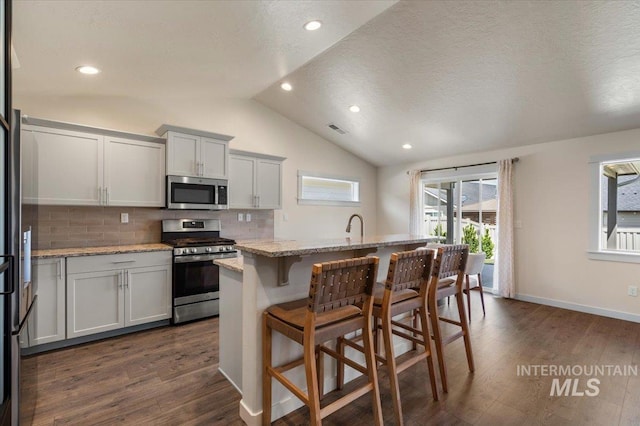 7682 W Itasco Dr, Boise, ID 83709 - kitchen with stainless steel appliances, vaulted ceiling, tasteful backsplash, a breakfast bar area, and light stone countertops