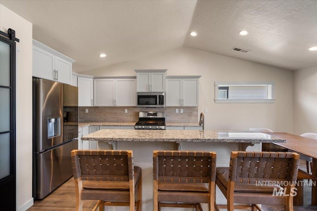 7682 W Itasco Dr, Boise, ID 83709 - kitchen with stainless steel appliances, vaulted ceiling, backsplash, a breakfast bar, and recessed lighting