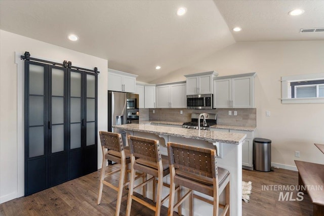 7682 W Itasco Dr, Boise, ID 83709 - kitchen featuring stainless steel appliances, vaulted ceiling, backsplash, a kitchen island with sink, and dark wood finished floors