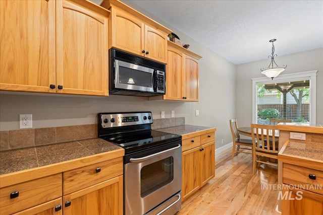 551 N Hannah Pl, Star, ID 83669 - kitchen featuring appliances with stainless steel finishes, tile countertops, light wood-type flooring, light brown cabinets, and decorative light fixtures