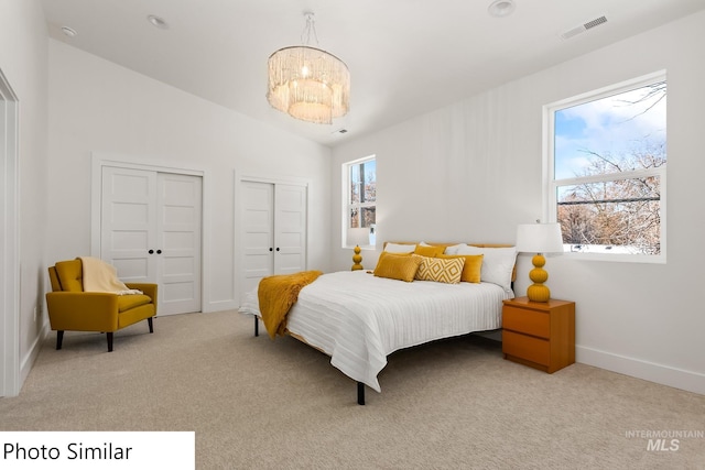 bedroom featuring lofted ceiling, a chandelier, light colored carpet, visible vents, and two closets