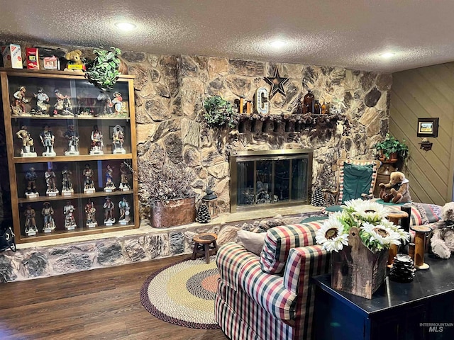 living room with wood walls, hardwood / wood-style floors, a stone fireplace, and a textured ceiling