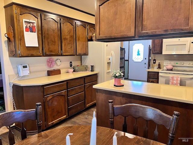 kitchen with white appliances, a kitchen breakfast bar, dark brown cabinets, and dark hardwood / wood-style floors